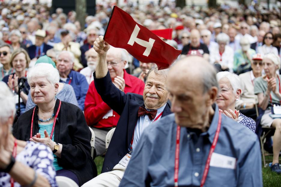 An audience member waves a Harvard flag on Harvard Alumni Day, 2025.